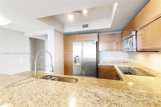 kitchen featuring kitchen peninsula, light stone counters, stainless steel appliances, a raised ceiling, and sink