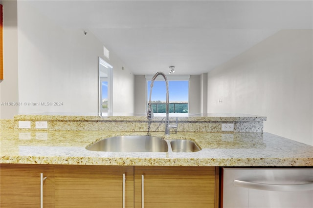 kitchen featuring dishwasher, light stone counters, and sink