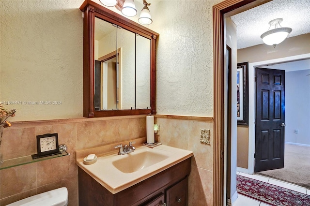 bathroom featuring vanity, toilet, a textured ceiling, and tile walls