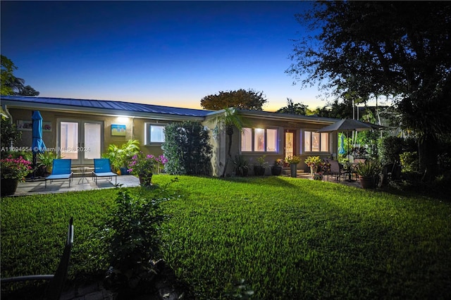 back house at dusk with french doors, a yard, and a patio