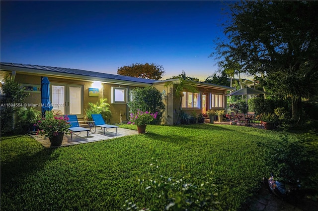 back house at dusk with a lawn and a patio