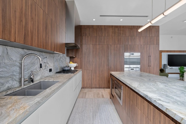 kitchen with backsplash, sink, appliances with stainless steel finishes, light hardwood / wood-style floors, and light stone counters