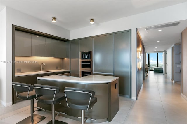 kitchen featuring sink, light tile patterned floors, a kitchen bar, a kitchen island, and appliances with stainless steel finishes