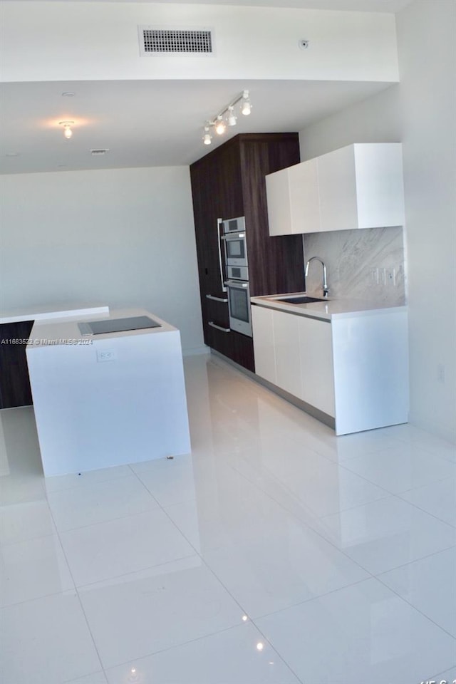 kitchen with decorative backsplash, stainless steel double oven, sink, light tile patterned floors, and white cabinetry