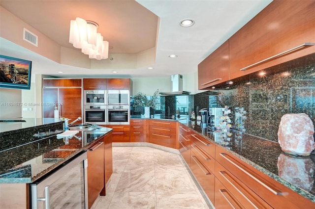 kitchen featuring dark stone counters, exhaust hood, double oven, and beverage cooler