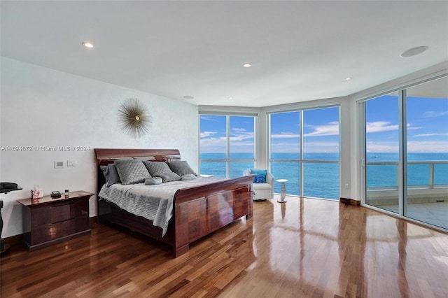 bedroom with hardwood / wood-style floors, a water view, expansive windows, and access to outside