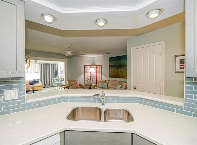 kitchen with backsplash, white cabinets, sink, crown molding, and ceiling fan