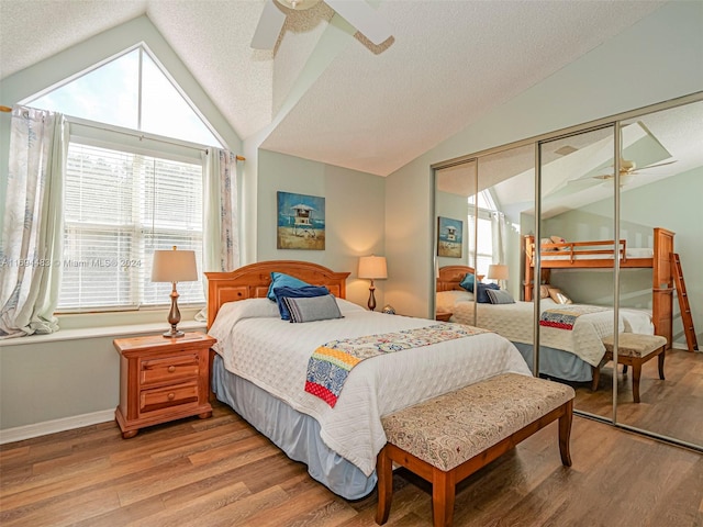 bedroom with ceiling fan, light hardwood / wood-style floors, a textured ceiling, vaulted ceiling, and a closet