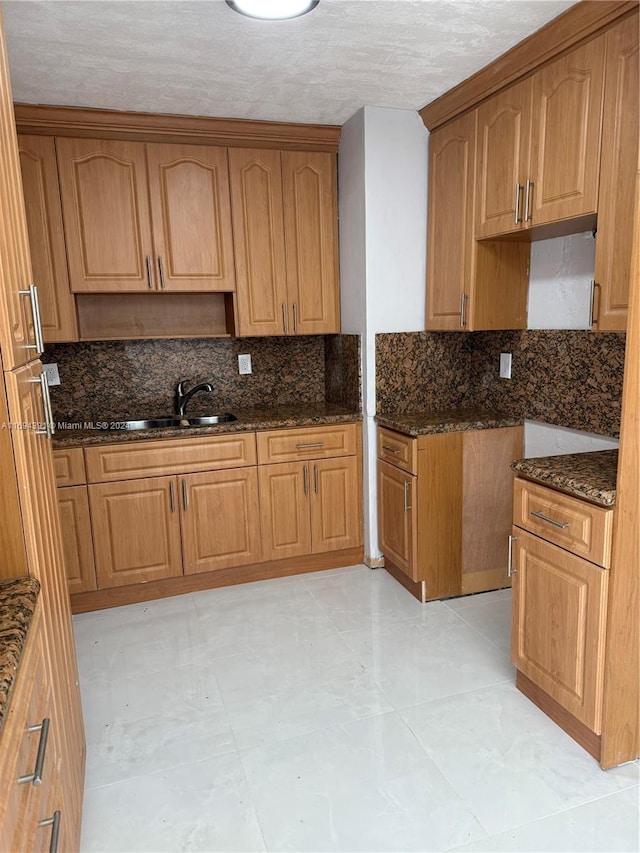 kitchen featuring tasteful backsplash, a textured ceiling, sink, light tile patterned floors, and dark stone countertops