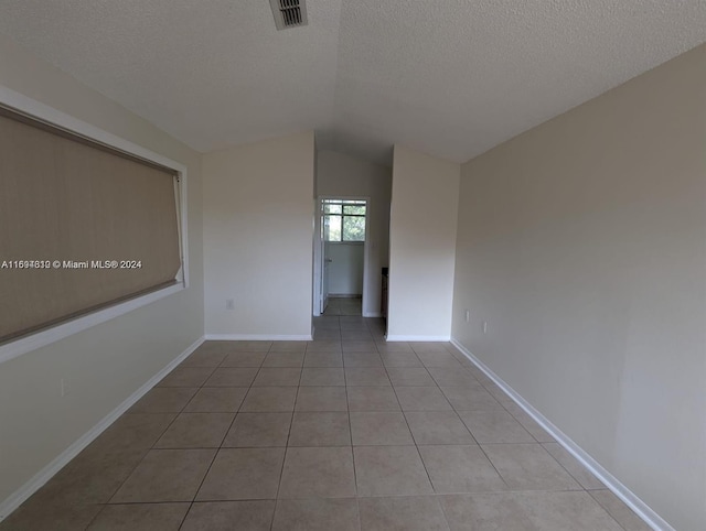 tiled empty room with a textured ceiling and lofted ceiling