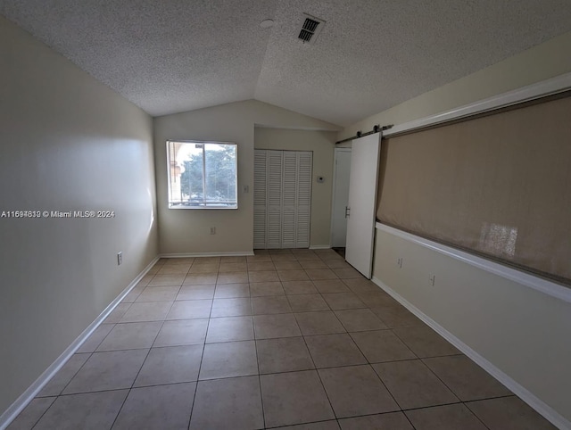 unfurnished room featuring a textured ceiling, a barn door, light tile patterned floors, and lofted ceiling