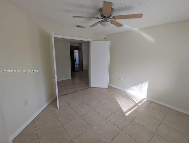 empty room with a textured ceiling, ceiling fan, and light tile patterned flooring