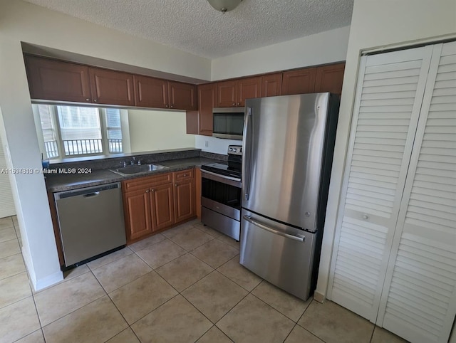 kitchen with light tile patterned flooring, appliances with stainless steel finishes, a textured ceiling, and sink