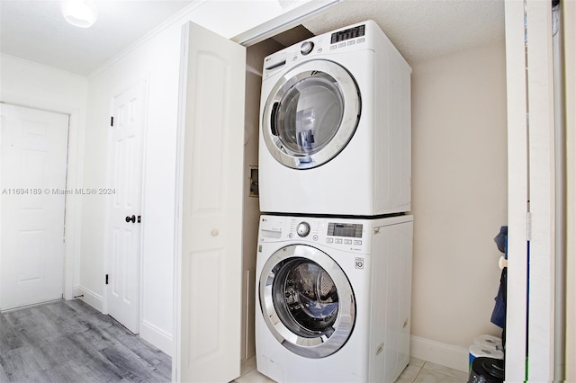 washroom featuring a textured ceiling, light wood-type flooring, stacked washer and dryer, and ornamental molding