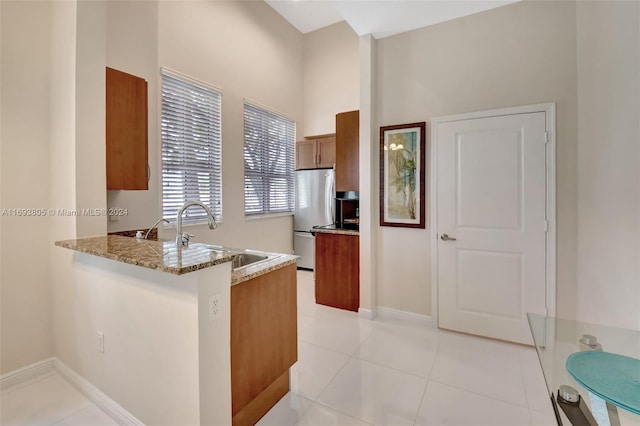 kitchen featuring kitchen peninsula, light stone countertops, sink, stainless steel refrigerator, and light tile patterned flooring