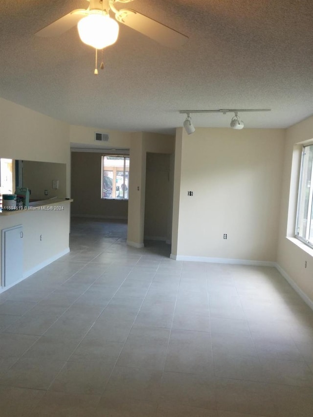 unfurnished living room featuring rail lighting, ceiling fan, light tile patterned floors, and a textured ceiling