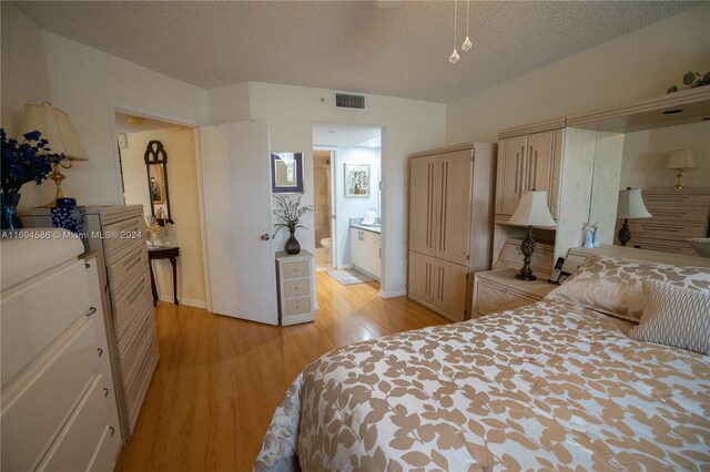 bedroom featuring ensuite bathroom, a textured ceiling, and light wood-type flooring