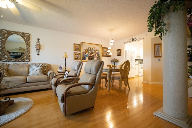 living room featuring ceiling fan, light hardwood / wood-style floors, a textured ceiling, and decorative columns