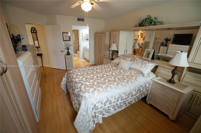 bedroom featuring ceiling fan, light hardwood / wood-style flooring, ensuite bathroom, and a textured ceiling