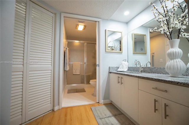 bathroom featuring hardwood / wood-style flooring, vanity, toilet, and a shower with shower door