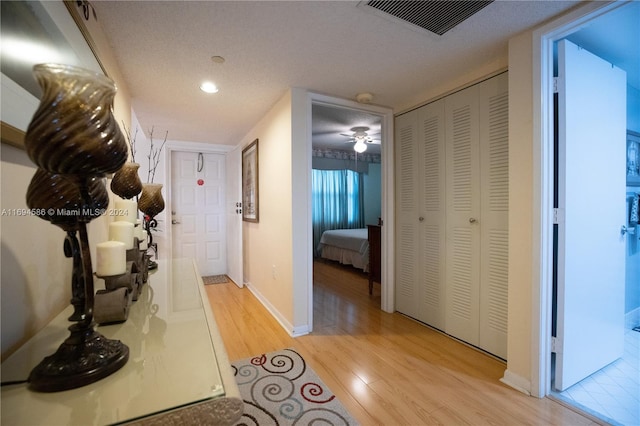 hallway with a textured ceiling and light hardwood / wood-style flooring