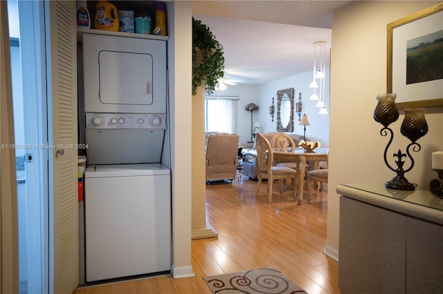 laundry area featuring a textured ceiling, light hardwood / wood-style flooring, and stacked washer / drying machine