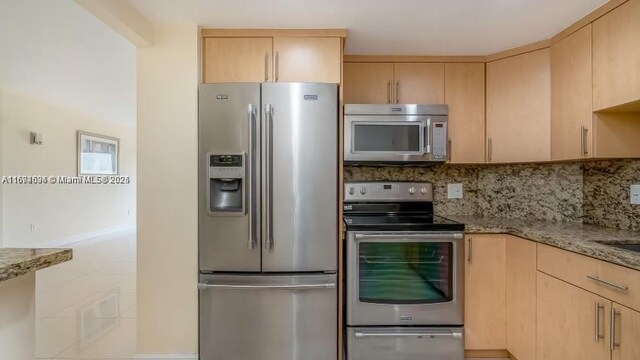 kitchen with tasteful backsplash, light stone counters, light brown cabinetry, and appliances with stainless steel finishes