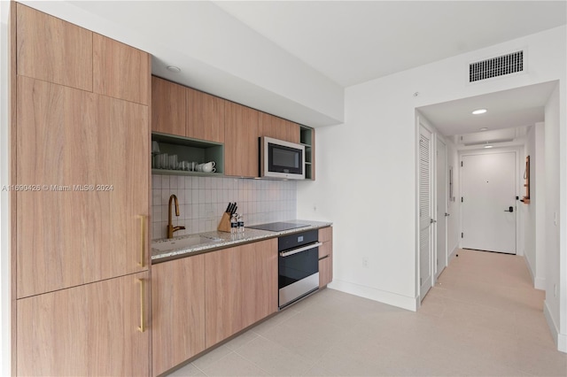 kitchen with appliances with stainless steel finishes, tasteful backsplash, light stone counters, sink, and light brown cabinets