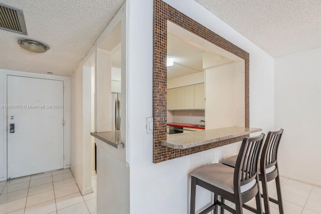 kitchen with stainless steel fridge, light tile patterned flooring, and a textured ceiling