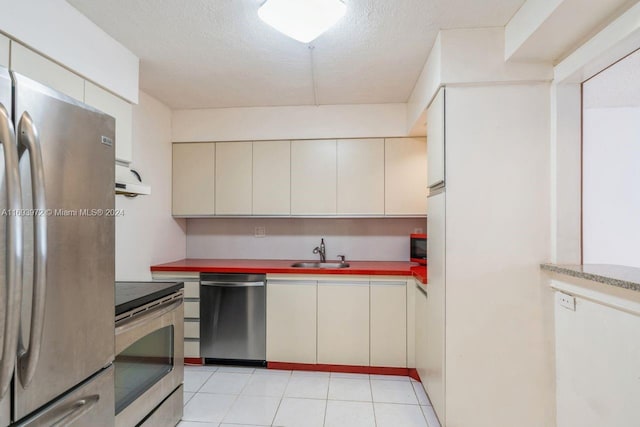 kitchen featuring appliances with stainless steel finishes, a textured ceiling, cream cabinets, and sink