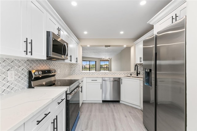 kitchen featuring light wood-type flooring, light stone counters, stainless steel appliances, sink, and white cabinets