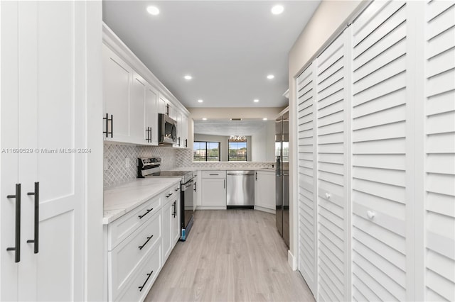 kitchen featuring stainless steel appliances, light stone counters, light hardwood / wood-style flooring, backsplash, and white cabinets