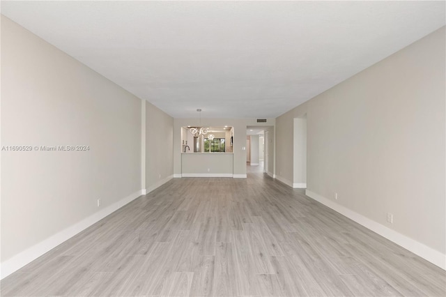 unfurnished living room featuring a notable chandelier and light hardwood / wood-style flooring