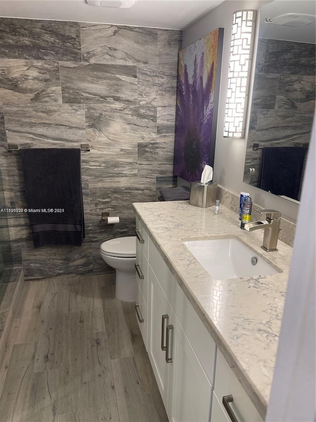 bathroom with wood-type flooring, vanity, toilet, and tile walls