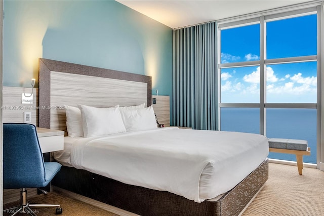 bedroom with carpet flooring, floor to ceiling windows, and a water view