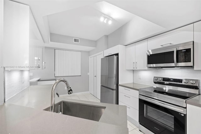 kitchen featuring appliances with stainless steel finishes, backsplash, sink, white cabinets, and light tile patterned flooring