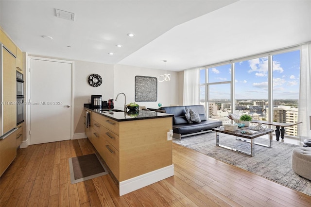 kitchen with kitchen peninsula, light brown cabinetry, sink, light hardwood / wood-style flooring, and a wall of windows