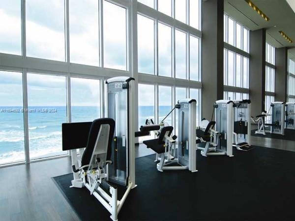 workout area featuring a water view, a high ceiling, and a wall of windows