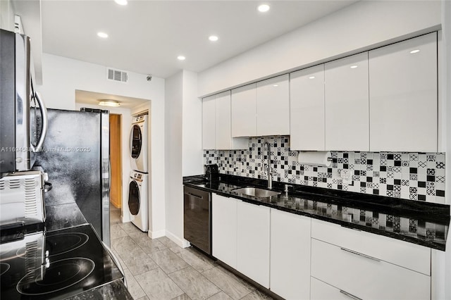 kitchen featuring stacked washer / drying machine, sink, dark stone countertops, dishwasher, and white cabinets