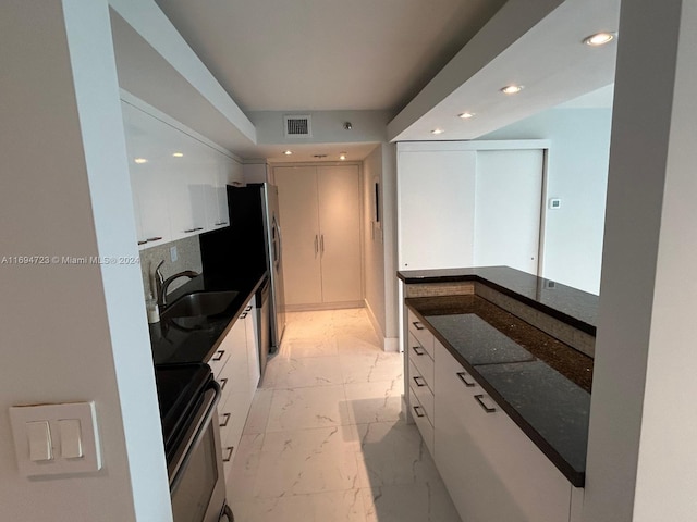 kitchen with white cabinetry, sink, dark stone counters, and range