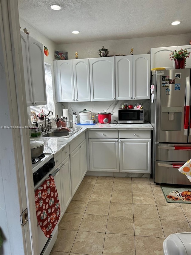 kitchen featuring sink, light tile patterned floors, a textured ceiling, appliances with stainless steel finishes, and white cabinetry