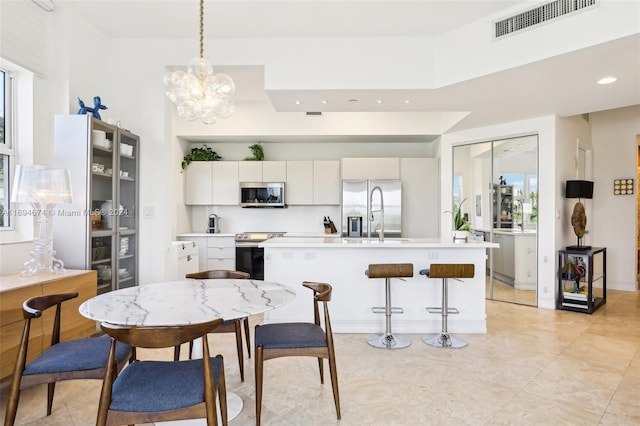 kitchen with stainless steel appliances, a kitchen island with sink, sink, decorative light fixtures, and white cabinetry