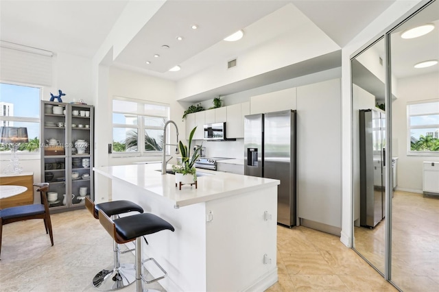 kitchen featuring sink, stainless steel appliances, a breakfast bar, white cabinets, and a center island with sink