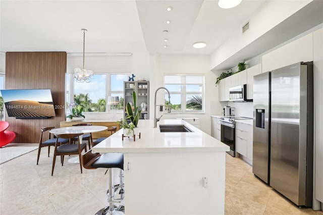 kitchen with sink, hanging light fixtures, an island with sink, white cabinetry, and stainless steel appliances