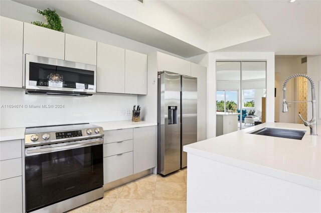 kitchen with appliances with stainless steel finishes, light tile patterned floors, white cabinetry, and sink