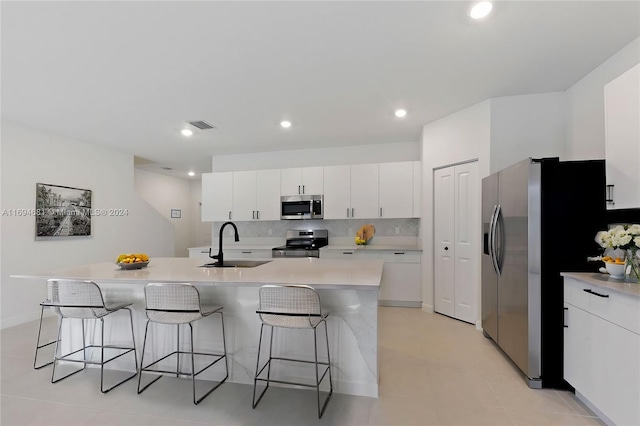 kitchen with sink, stainless steel appliances, a breakfast bar area, a center island with sink, and white cabinets