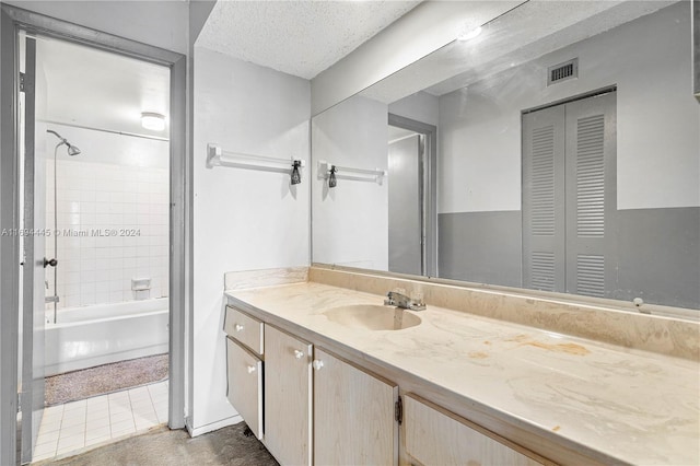 bathroom with tile patterned flooring, vanity, tiled shower / bath, and a textured ceiling