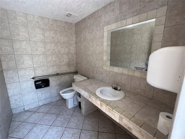 bathroom with tile patterned floors, a textured ceiling, sink, tile walls, and toilet