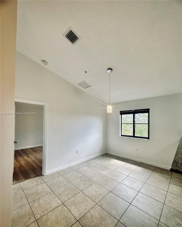 tiled empty room featuring vaulted ceiling