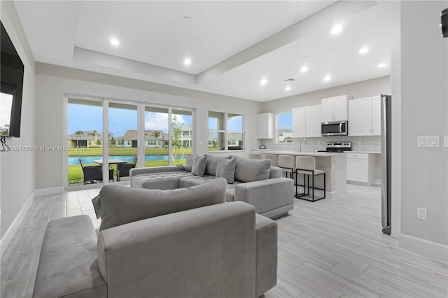 living room featuring sink, a tray ceiling, and light hardwood / wood-style flooring